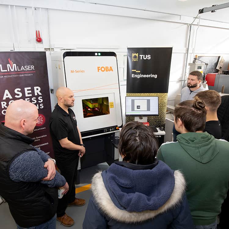 a group of people standing around a FOBA laser marking machine