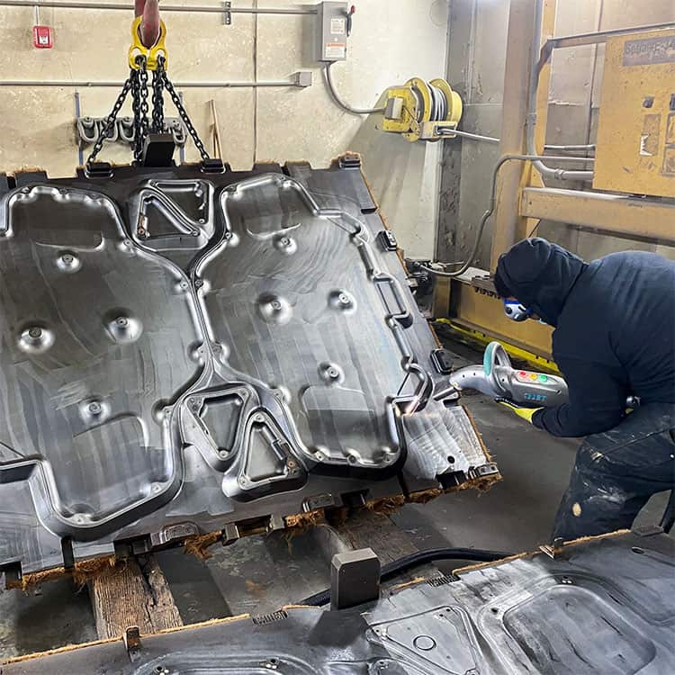 Wide angle picture of a man using a laser cleaning machine to remove contamination from a large mould tool